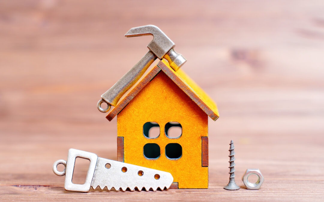 Miniature wooden house and a set of small-scale hand tool replicas and fasteners isolated on a wooden background. Home renovation related concept.